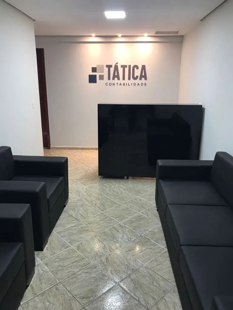 Recepção da Tática Contabilidade, com sofás pretos e o logo do escritório na parede